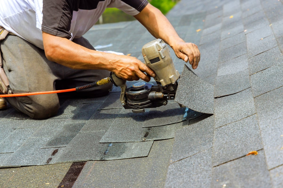 Professional roofing contractor installing shingles on a residential roof with a nail gun, created as an independent concept for a Roofing Company website