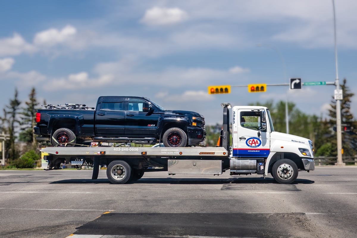 Flatbed tow truck transporting a vehicle through a city intersection for Floral City Towing