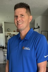 Man smiling indoors wearing blue polo shirt with plumbing company logo and Nike swoosh